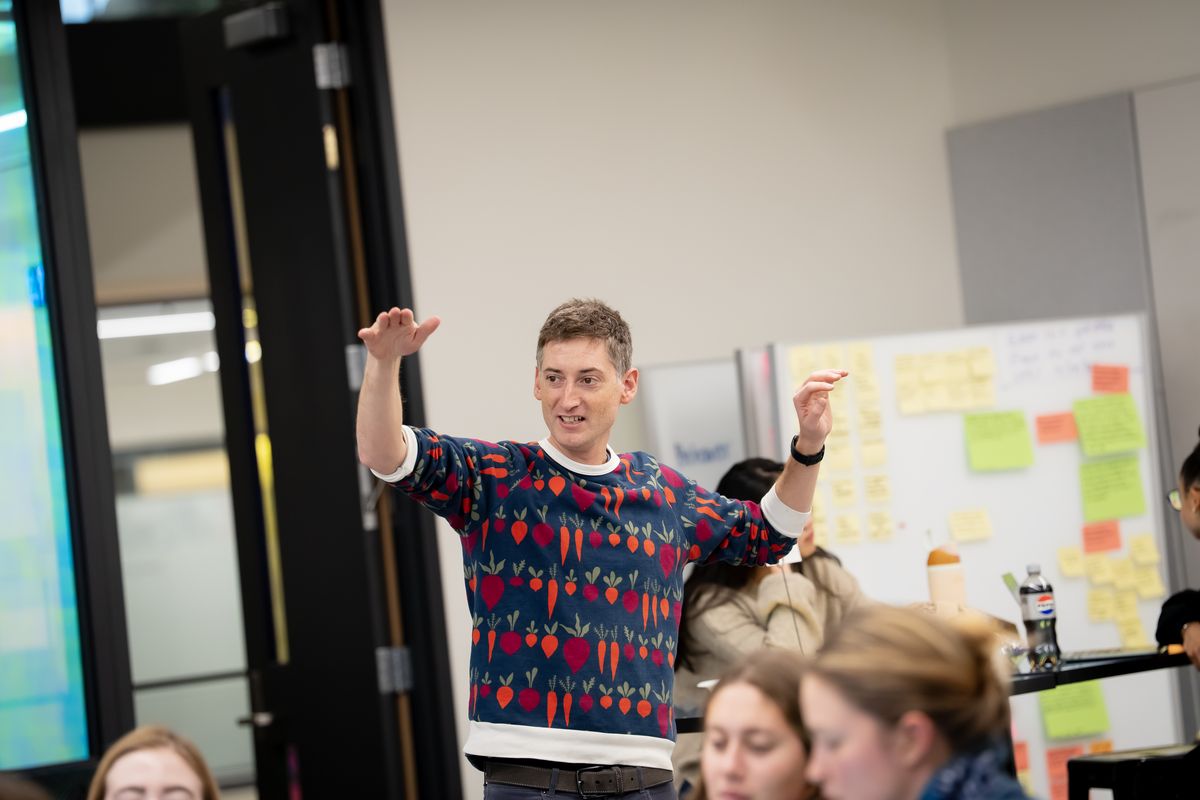 Professor Rafe Steinhauer mid-gesture, teaching in front of a wall of sticky notes